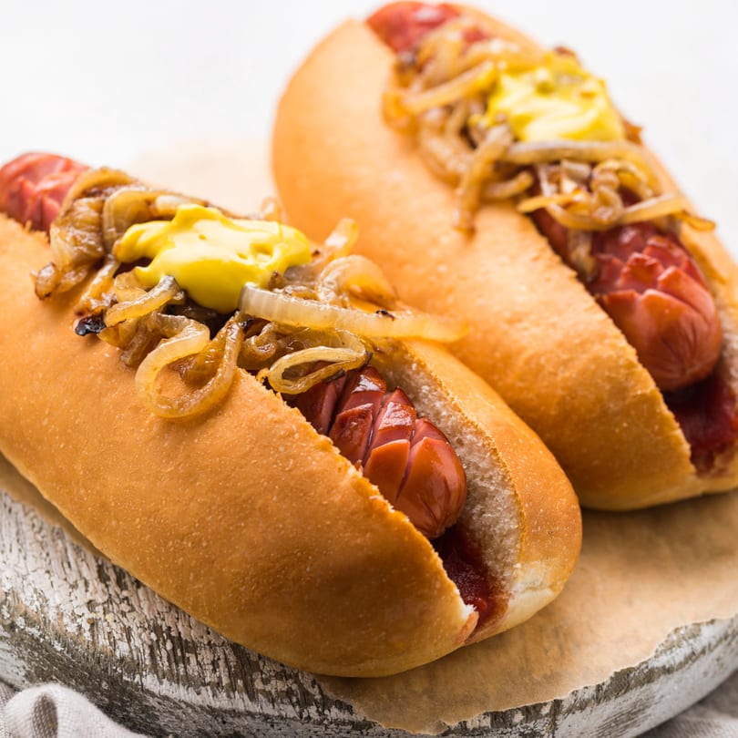 Two hot dogs with grilled onions and mustard on buns, served on a wooden board.