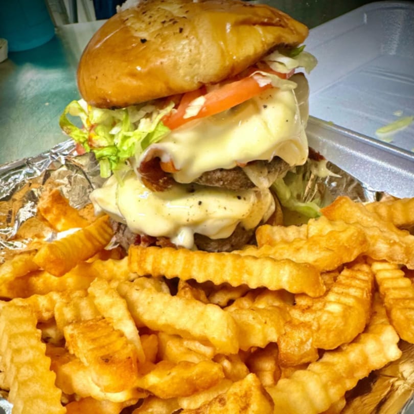 A double cheeseburger with melted cheese, lettuce, and tomato, served with crinkle-cut fries.