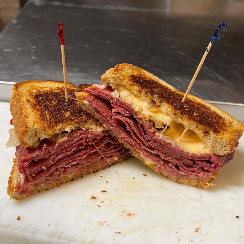 A Rick's Cheese Steak Shop sandwich, cut in half, revealing layers of meat and melted cheese.