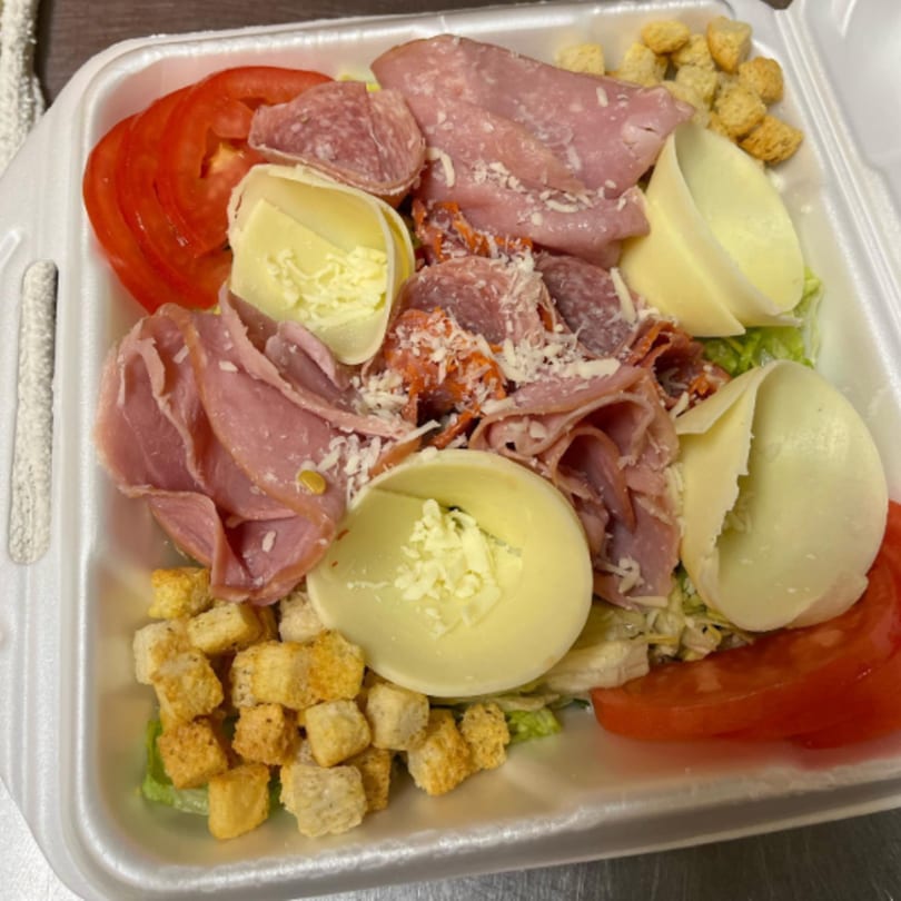 A chef salad with ham, salami, cheese, tomatoes, and croutons in a white takeout container.