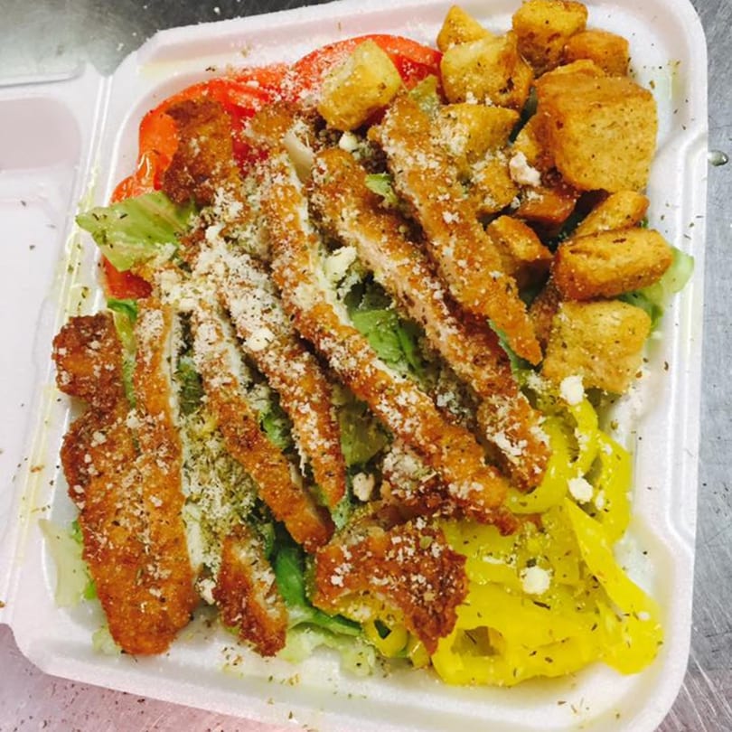 Chicken Caesar salad with croutons, tomatoes, and yellow peppers in a white takeout container.