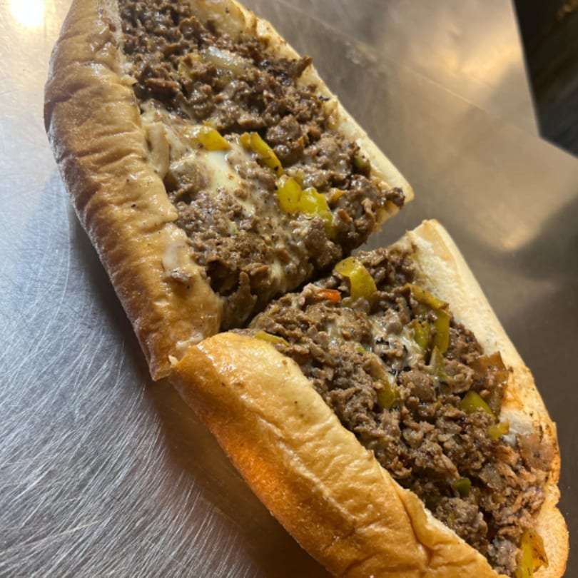 A Rick's Cheese Steak Shop cheesesteak, cut in half, with melted cheese and green peppers.